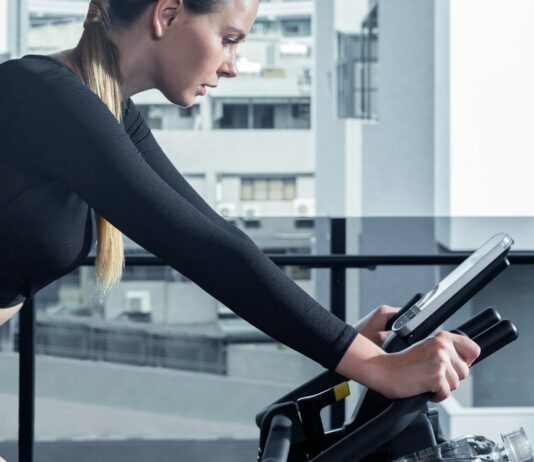 실내에서 즐기는 유산소 운동의 장점 a woman on a stationary bike using a tablet