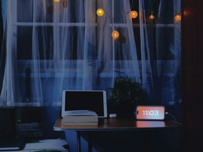 Desk with tablet, book, and digital clock at night.